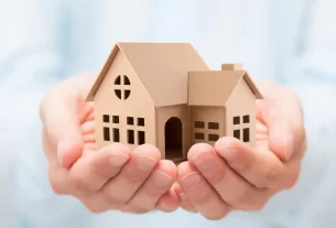 Imagem ilustrativa de proteção patrimonial com imóvel sendo segurado por mãos humanas