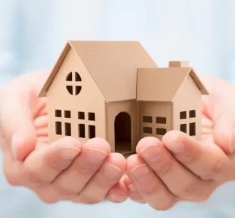 Imagem ilustrativa de proteção patrimonial com imóvel sendo segurado por mãos humanas